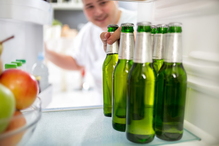 Boy take bottle of cold beer from refrigeratorの写真素材