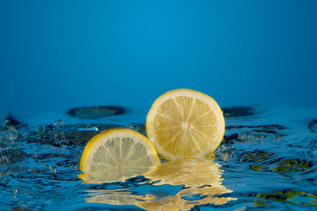 yellow lemon dropped into water backgroundの写真素材