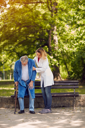 Nurse helping elderly disabled man outdoorの写真素材