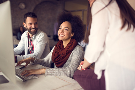 Smiling Afro-American girl working on computer in group in officeの写真素材
