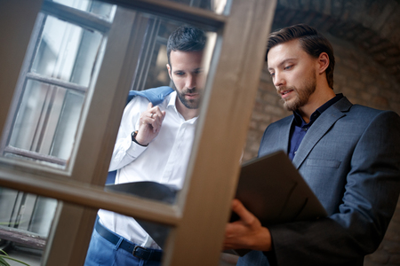 Two young businessmen in office near window reading business planの写真素材