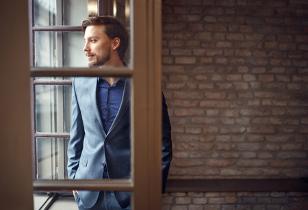 Man in business suit looking through window in officeの写真素材