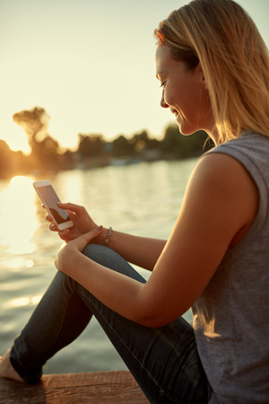 Woman on dock looking at cellphone at sunsetの写真素材