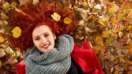 Ginger woman lying on leaves in park in autumn, top view