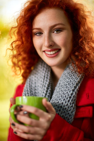 Woman holding cup of tea in park in autumnの写真素材