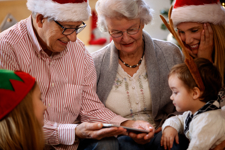 Happy grandparents with children looking Christmas photos on cell phoneの写真素材