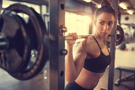 Young female doing exercise with barbell in fitness clubの写真素材