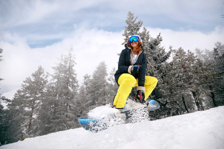 smiling girl snowboarder in jump at ski resort in the mountainの写真素材