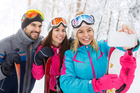 Young woman with friends taking selfie on skiing in mountainの写真素材