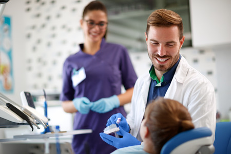 Smiling dentist shows properly brushing teeth on model of teeth in jaw to young patient の写真素材