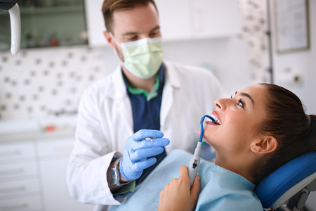 Beautiful young female with dental sucker on chair in ordination の写真素材