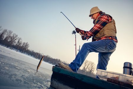 Elderly fisherman catch fish on the frozen river in winterの写真素材