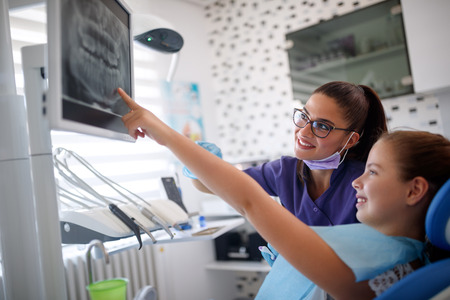 Girl in dental chair showing to female dentist her tooth on dental x-rayの写真素材