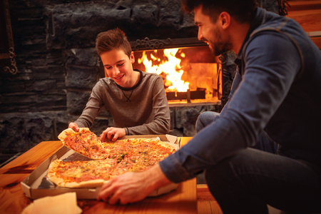 Smiling father and son eating pizza together for dinnerの写真素材