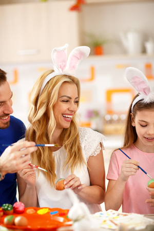 Happy mother with daughter and husband painting Easter eggsの写真素材