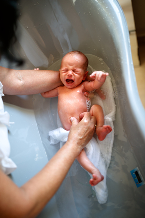 Little newborn baby crying while bathing in bathtubの写真素材