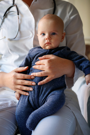 Cute male baby sits in pediatrician lapの写真素材