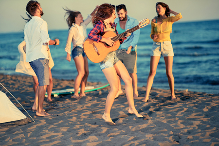 Summer, holidays, vacation, music, happy people concept - happy young people dancing together at the beach on beautiful summer sunsetの写真素材