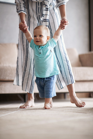 Adorable baby boy making first steps with mother at homeの写真素材