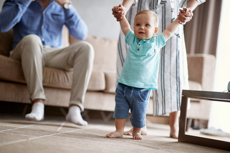 Happy family -Smiling baby boy learning walking with mother, child enjoys the first stepsの写真素材
