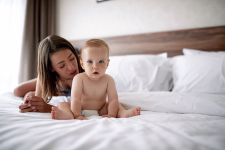Happy mother with cute baby boy on the bed in the roomの写真素材