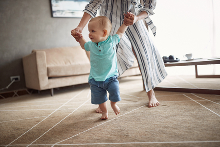 Cute baby boy learning walking with mother, child enjoys the first stepsの写真素材