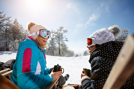Two female skiers talking with drink in sunbed on ski terrainの写真素材