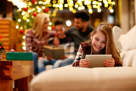 Cute little girl with headphones is using a tablet and smiling on Christmas dayの写真素材