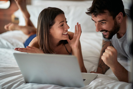 Funny in bed - Happy young couple with laptop in the bedの写真素材
