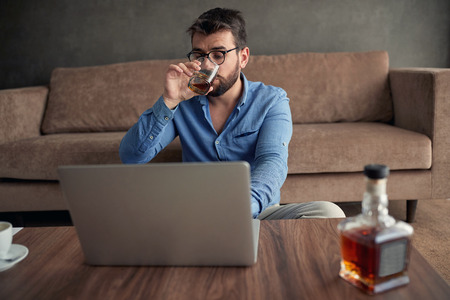 businessman is drinking whisky while working from a home at laptopの写真素材