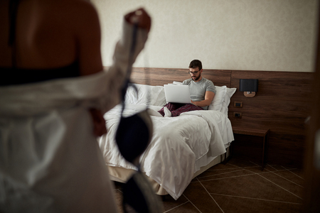 Young couple in the bedroom, man holding a laptop computer and workingの写真素材