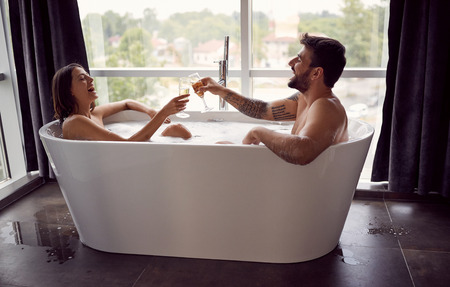 Smiling young boy and girl have fun together in the bathtub and drinking champagneの写真素材