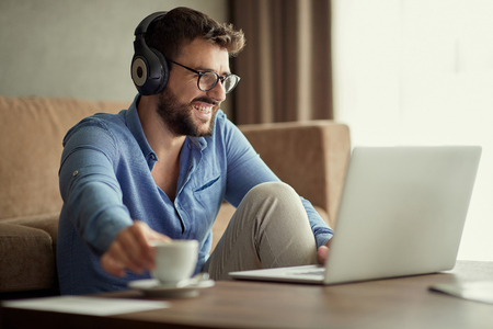 Smiling man uses a laptop to listen to music and relax at homeの写真素材