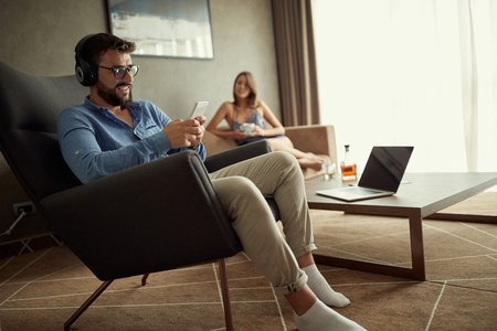 Smiling man uses a phone with headphones to listen to music and relax at homeの写真素材
