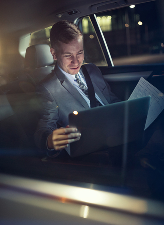smiling businessman in moving car checking his working on laptopの写真素材