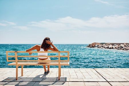 young woman watching the sea sitting on a bench and relaxの写真素材