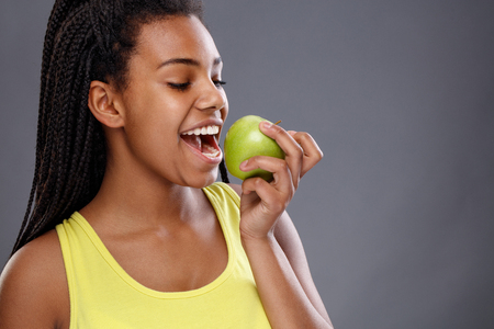 Afro-American female biting apple with beautiful teethの写真素材