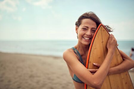 Smiling surfer girl posing with her surfboard on the beach.