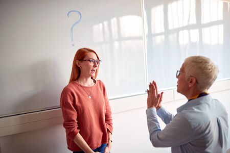 Professor explaining and questioning young student in classroom on board
