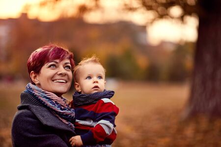 Happy beautiful mother with son at the autumn park enjoying togetherの写真素材