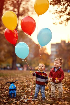 Happy little boys playing together on the autumn park with balloonsの写真素材