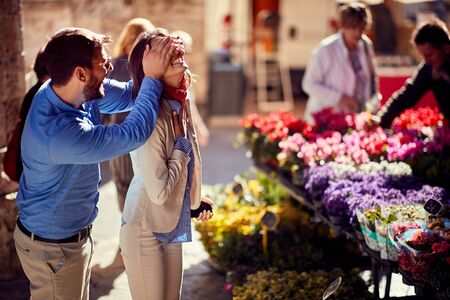 Man surprises happy woman at flower shop on the street.