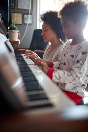 Christmas, winter holidays, new year party and family concept.young mother with child  play music on piano.の写真素材