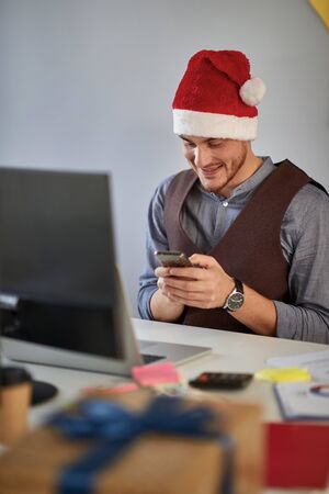 Young business man in santa hat working at a computer at Christmas  at office.