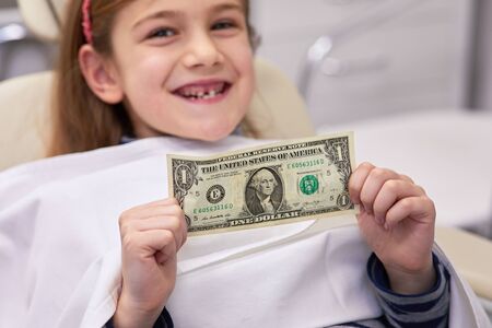 Cute kid holding one dollar bill and showing her missing tooth with a smile