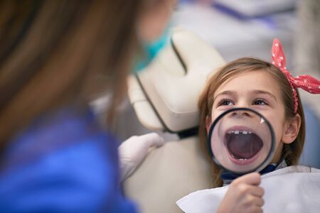 Little girl in dental office with opened magnified mouth