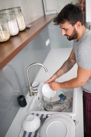 Young man washes dishes after breakfast in  pajamas.の写真素材