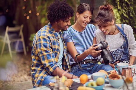 group of young smiling friends looking to camera and talking about photos and photography outdoorの写真素材