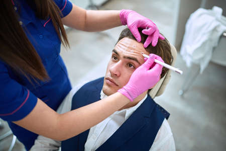 Aesthetic surgion marks point on male patients forhead