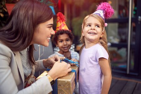 A female brunette opening  birthday presents to a little girl looking away, smiling